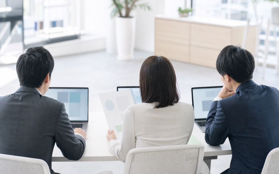 会議テーブルで3人がノートPCを囲んで打ち合わせをする様子（イメージ）